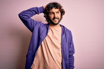 Young handsome sporty man with beard wearing casual sweatshirt over pink background smiling confident touching hair with hand up gesture, posing attractive and fashionable