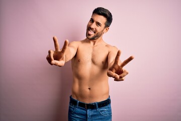 Fototapeta premium Young handsome strong man with beard shirtless standing over isolated pink background smiling with tongue out showing fingers of both hands doing victory sign. Number two.