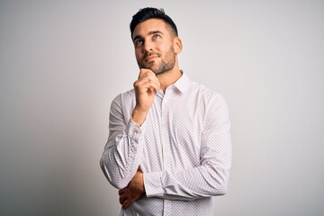 Young handsome man wearing elegant shirt standing over isolated white background with hand on chin thinking about question, pensive expression. Smiling and thoughtful face. Doubt concept.
