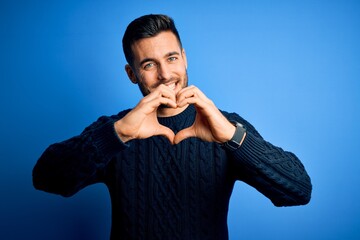 Young handsome man wearing casual sweater standing over isolated blue background smiling in love doing heart symbol shape with hands. Romantic concept.