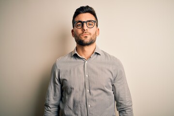 Obraz premium Young handsome man wearing elegant shirt and glasses over isolated white background Relaxed with serious expression on face. Simple and natural looking at the camera.