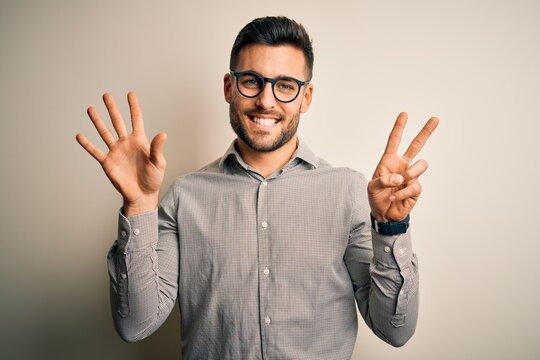 Young handsome man wearing elegant shirt and glasses over isolated white background showing and pointing up with fingers number seven while smiling confident and happy.