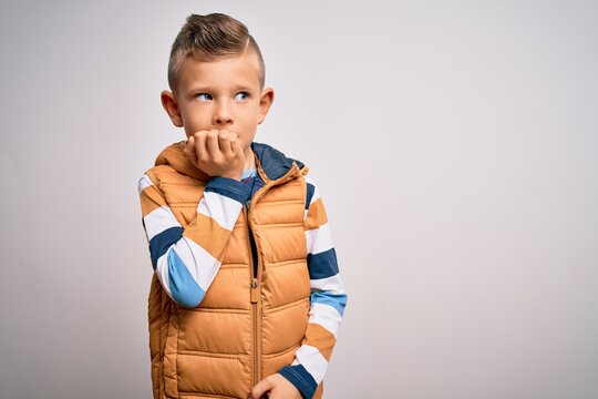 Young little caucasian kid with blue eyes standing wearing winter coat over isolated background looking stressed and nervous with hands on mouth biting nails. Anxiety problem.