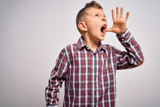 Young little caucasian kid with blue eyes wearing elegant shirt standing over isolated background shouting and screaming loud to side with hand on mouth. Communication concept.