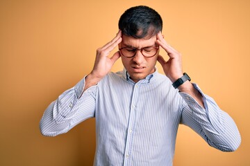 Young handsome hispanic business man wearing nerd glasses over yellow background with hand on head...