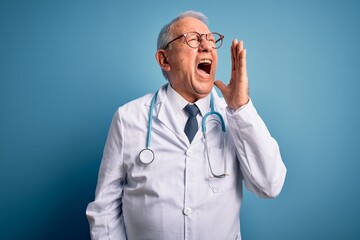 Senior grey haired doctor man wearing stethoscope and medical coat over blue background shouting and screaming loud to side with hand on mouth. Communication concept.