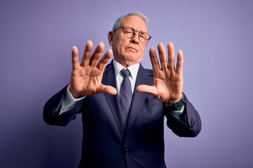 Grey haired senior business man wearing glasses and elegant suit and tie over purple background doing frame using hands palms and fingers, camera perspective
