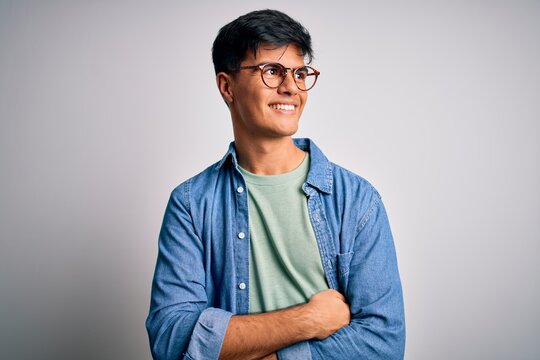 Young handsome man wearing casual shirt and glasses over isolated white background looking away to side with smile on face, natural expression. Laughing confident.