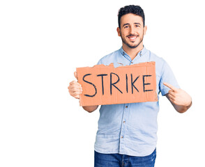 Young hispanic man holding strike banner cardboard smiling happy pointing with hand and finger
