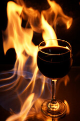 Obraz na płótnie Canvas glass of red wine on glass table with fire around it on black background, romantic photo