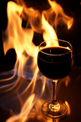 glass of red wine on glass table with fire around it on black background, romantic photo