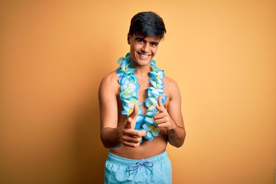 Young handsome tourist man on vacation wearing swimwear and hawaiian lei flowers pointing fingers to camera with happy and funny face. Good energy and vibes.