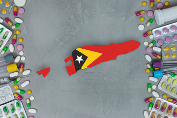 The East Timor State began research for treatment and medicine to combat the pandemic outbreak disease coronavirus. Medicine, pills, needles, syringes and East Timor map and flag on gray background.