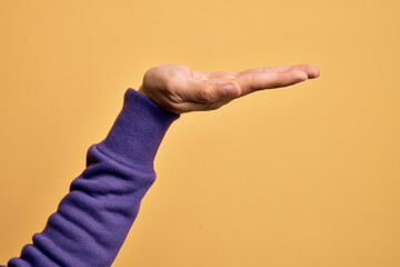 Hand of caucasian young man showing fingers over isolated yellow background with flat palm presenting product, offer and giving gesture, blank copy space