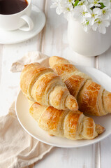 Delicious breakfast with croissants and coffee and spring flowers on the white wooden table