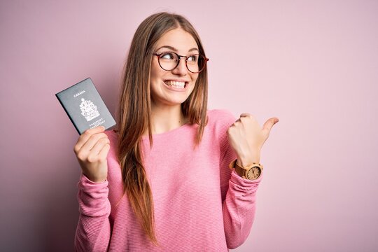 Beautiful redhead tourist woman holding canadian canada passport over pink bakcground pointing and showing with thumb up to the side with happy face smiling