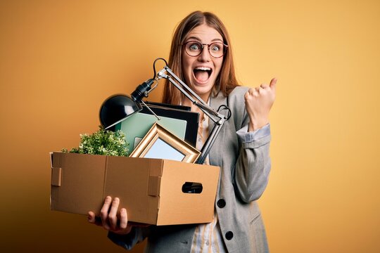 Young beautiful redhead businesswoman fired holding carboard box over yellow background screaming proud and celebrating victory and success very excited, cheering emotion