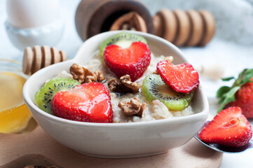 Breakfast with oatmeal with strawberries, kiwi, honey, walnuts and egg on white background. Breakfast for child. Oatmeal in a white heart-shaped plate