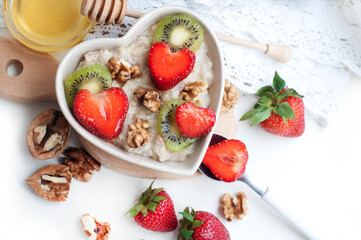Breakfast with oatmeal with strawberries, kiwi, honey, walnuts and egg on white background. Breakfast for child. Oatmeal in a white heart-shaped plate. Top view