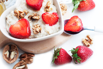 Breakfast with oatmeal with strawberries, honey, walnuts and egg on white background. Breakfast for child. Oatmeal in a white heart-shaped bowl