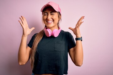 Young beautiful fitness sports woman wearing training cap and headphones over pink background...