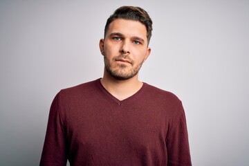 Fototapeta premium Young man with blue eyes wearing casual sweater standing over isolated background with serious expression on face. Simple and natural looking at the camera.