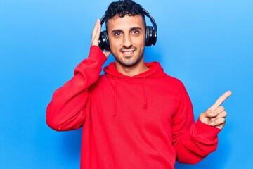 Naklejka premium Young hispanic man listening to music using headphones smiling happy pointing with hand and finger to the side