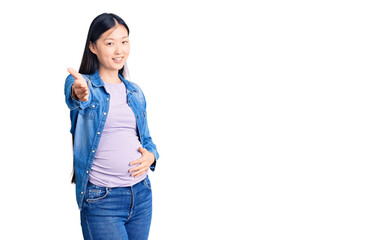 Young beautiful chinese woman pregnant expecting baby smiling cheerful offering palm hand giving assistance and acceptance.