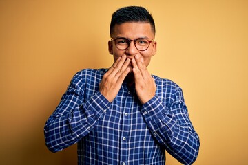 Young handsome latin man wearing casual shirt and glasses over yellow background laughing and...