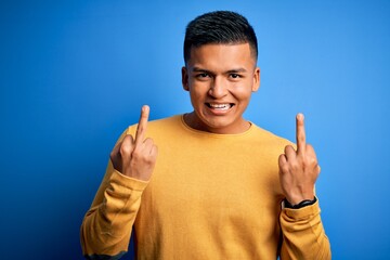 Young handsome latin man wearing yellow casual sweater over isolated blue background Showing middle...