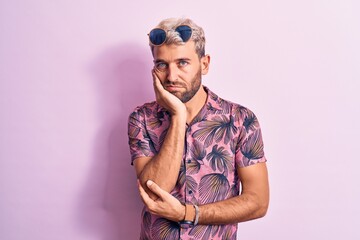 Handsome blond man on vacation wearing casual shirt and sunglasses over pink background thinking looking tired and bored with depression problems with crossed arms.