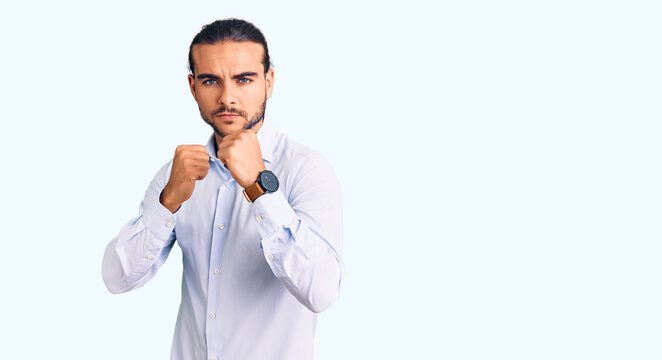 Young handsome man wearing business clothes ready to fight with fist defense gesture, angry and upset face, afraid of problem