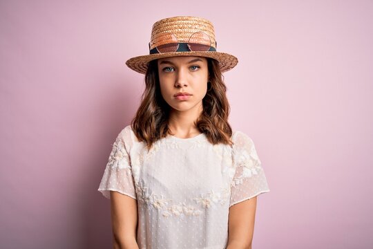 Young beautiful blonde girl wearing summer hat over pink isolated background with serious expression on face. Simple and natural looking at the camera.
