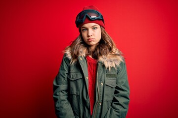 Young blonde girl wearing ski glasses and winter coat for ski weather over red background depressed and worry for distress, crying angry and afraid. Sad expression.