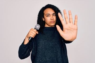 Young african american curly singer woman singing using microphone over white background with open hand doing stop sign with serious and confident expression, defense gesture