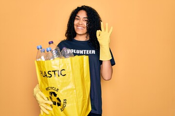 Young african american woman doing volunteering recycling holding bag with plastic bottles doing ok sign with fingers, excellent symbol