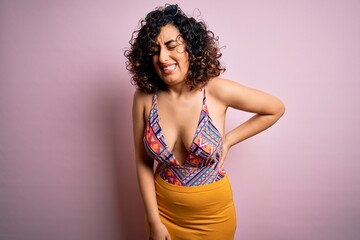 Young beautiful arab woman on vacation wearing swimsuit and sunglasses over pink background Suffering of backache, touching back with hand, muscular pain