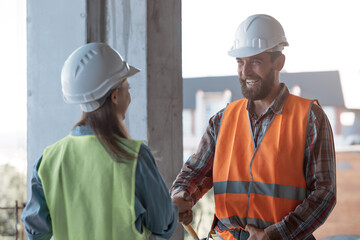 A Caucasian bearded worker in a protective helmet and orange vest shakes hands with a quality...