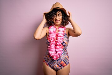 Young beautiful arab woman on vacation wearing swimsuit and hawaiian lei flowers suffering from headache desperate and stressed because pain and migraine. Hands on head.