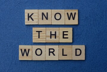 phrase know the world  in small square wooden letters with black font on a blue background