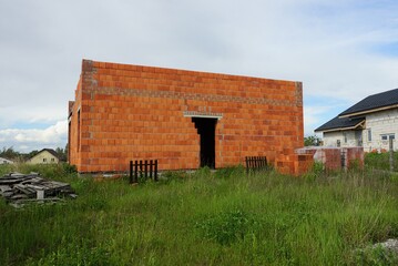 unfinished red brick house in green grass against the sky