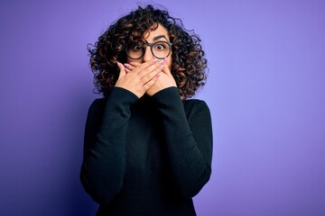 Young beautiful curly arab woman wearing casual sweater and glasses over purple background shocked covering mouth with hands for mistake. Secret concept.