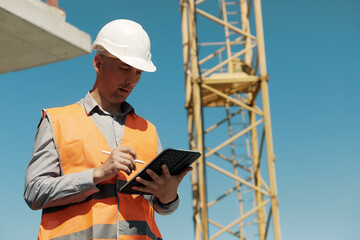 An engineer in an orange vest and a white construction control helmet conducts an inspection with a...