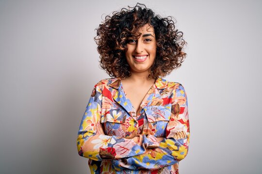 Young beautiful curly arab woman wearing floral colorful shirt standing over white background happy face smiling with crossed arms looking at the camera. Positive person.
