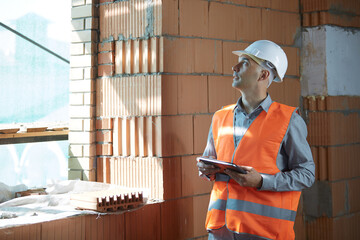 An engineer in an orange vest and white construction control helmet conducts an inspection with a...