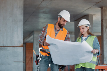 Construction industry maintenance engineer a pretty girl dressed in a uniform and protective helmet discusses a construction plan with a worker. Concentrated builders working together on a project