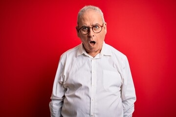 Middle age handsome hoary man wearing casual shirt and glasses over red background afraid and shocked with surprise and amazed expression, fear and excited face.