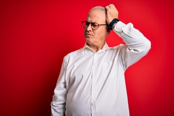 Fototapeta premium Middle age handsome hoary man wearing casual shirt and glasses over red background confuse and wondering about question. Uncertain with doubt, thinking with hand on head. Pensive concept.