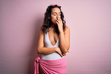 Beautiful woman with curly hair on vacation wearing white swimsuit over pink background bored yawning tired covering mouth with hand. Restless and sleepiness.