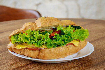 Fresh croissant with ham and lettuce on a wooden table in a cafe.